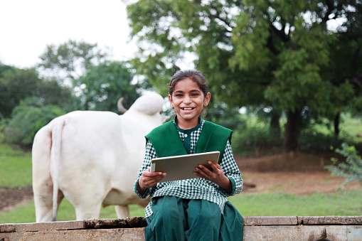 Little school girl sitting on ox cart and holding digital tablet with smiley face.  