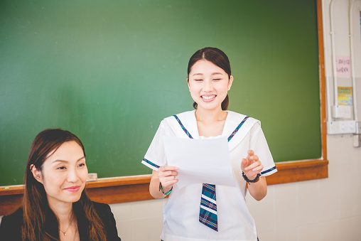 Beautiful female Chinese student satisfied about her exam results, Hong Kong, Asia.  Mid adult teacher is happy too. Nikon D800, full frame, XXXL.