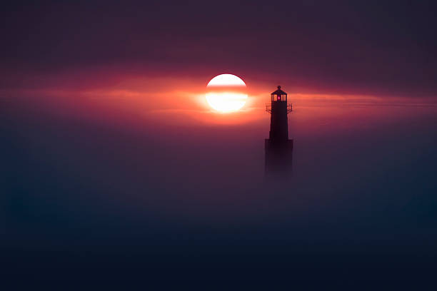 Amazing scenic lighthouse with rising sun peeking through dense fog