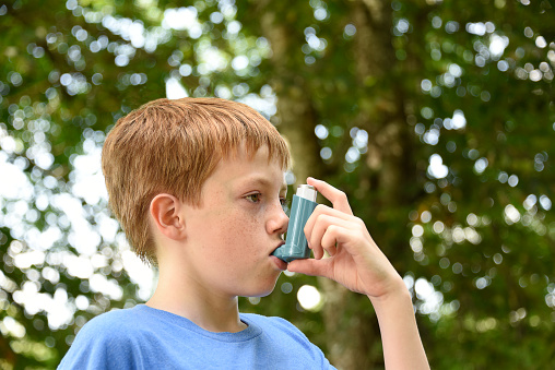 Young boy using a blue asthma inhaler whilst outdoors.