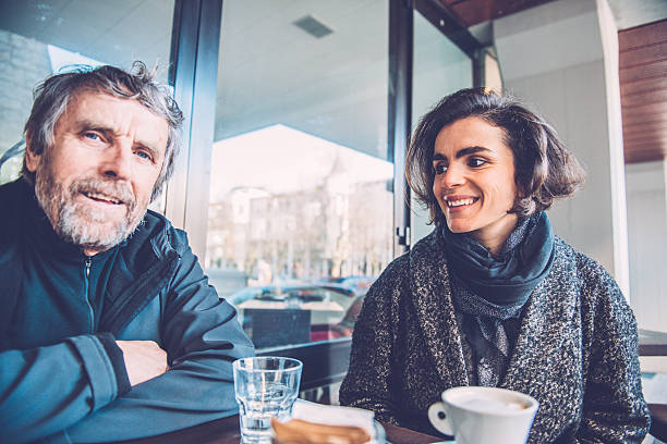 Pretty adult woman and senior man are having coffee in front of a new modern Coffee Shop Caffe Trieste in Nova Gorica and enjoying their conversation, Slovenia, Europe. The man is looking at the camera. Winter. Copy space. Nikon D800, full frame, XXXL.