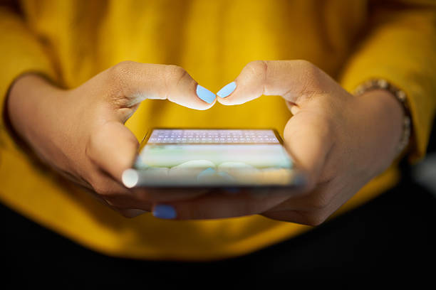 Woman Typing Phone Message On Social Network At Night Young woman using cell phone to send text message on social network at night. Closeup of hands with computer laptop in background text messaging photos stock pictures, royalty-free photos & images