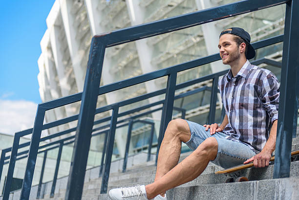 istock Cheerful young guy relaxing on staircase with skateboard 598925378
