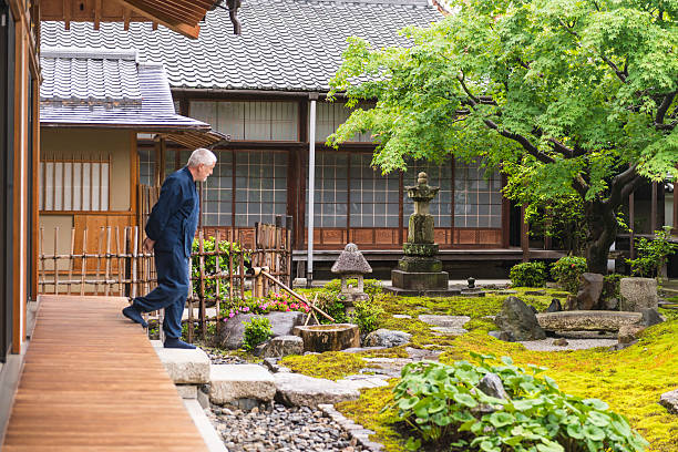Senior man on temple garden Senior man in dark blue kimono walking from wooden porch outside of a temple building on the temple garden. Side view. In garden that is surrounded with temple buildings are green trees, moss and stones. Japan. walking into glass door stock pictures, royalty-free photos & images