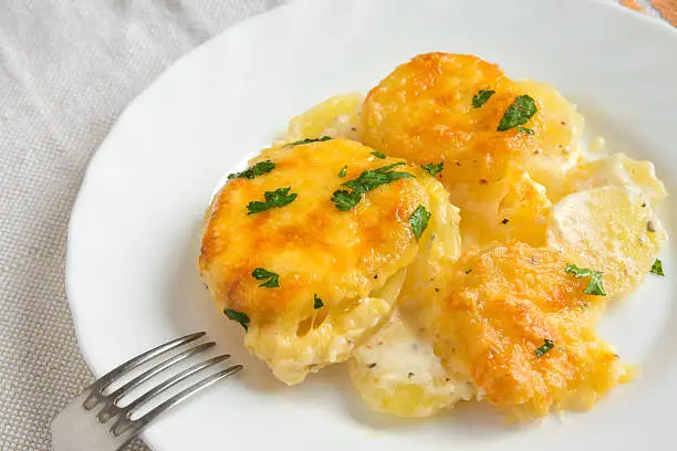 Potato gratin (casserole) with cream, cheese and parsley on white plate
