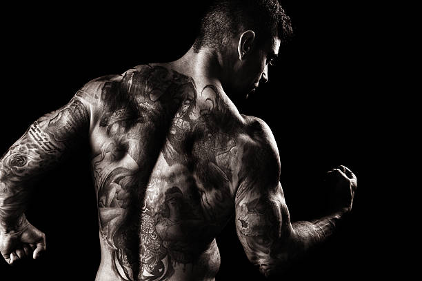 Muscular, Fully Tatooed Male Back Flexing A muscular, fully tattooed man flexing white facing away from the camera, shot in studio against a black background. forearm tattoos men stock pictures, royalty-free photos & images