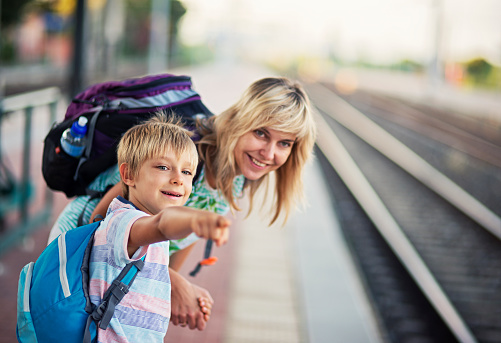 Mother with son on train station watching the incoming train. The boy aged 7 is pointing at the train and both are smiling, Small italian train station in Tuscany.