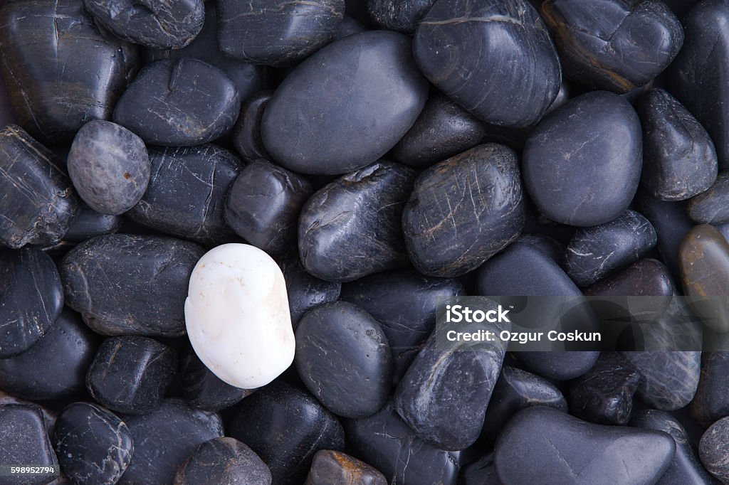 Individuality concept Individuality concept with a full frame background of weathered smooth black basalt pebbles with a single different white quartz stone Awe Stock Photo