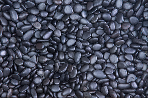 Background texture of small smooth waterworn black pebbles or stones for use in decor and garden landscaping, full frame close up view from above