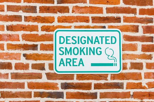 A sign letting people that smoking is allowed in this immediate area.  The designated smoking area sign is secured to a red brick wall.