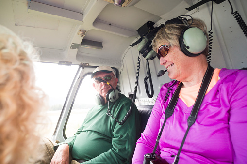 Smiling senior woman wearing headset in helicopter is excited to fly with her husband, Juneau, Alaska, USA