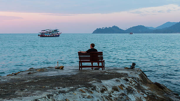 istock Man sits alone on a bench on the seafront promenade. 599104630