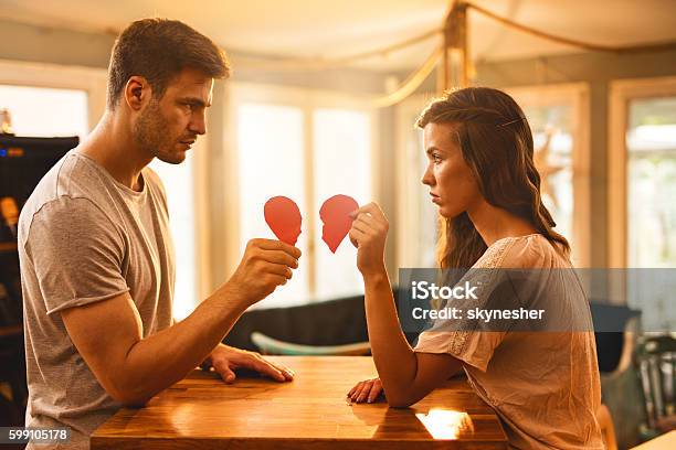 Young Couple With Broken Heart Shape Looking At Each Other Stock Photo - Download Image Now