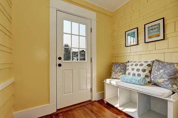 Entryway with yellow walls and storage bench in white with colorful pillows.Northwest, USA