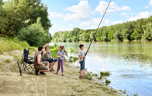 family camping and fishing, people active in nature, child caught fish on bait, river and forest, summer season