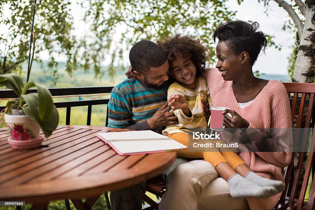 Playful African American family having fun on a terrace. Cheerful black family relaxing on a balcony and having fun together while father is tickling small girl. Adult Stock Photo
