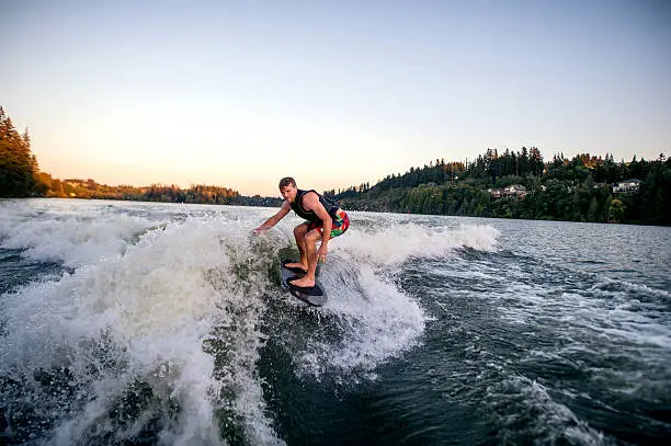 Athletic adult male wake surfing behind a ski boat on a lake
