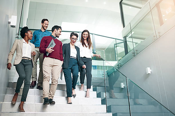 The end of another successful business day Shot of a group of colleagues talking together while walking down stairs in a large modern office steps photos stock pictures, royalty-free photos & images