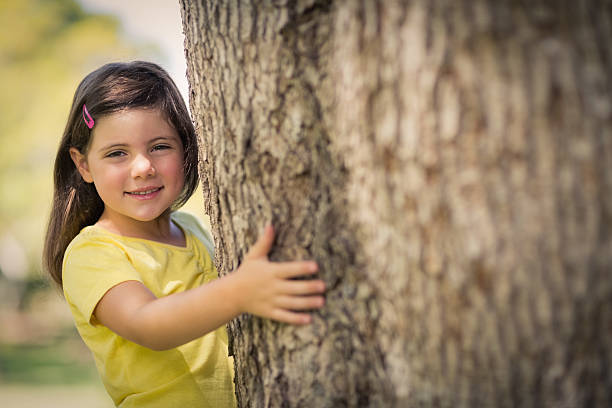 istock Smiling girl hugging  tree trunk in park 599112292