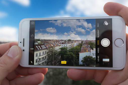 Berlin, Germany - September 4, 2016: Hands holding Iphone 6, using camera app to take a HDR picture of a city skyline.