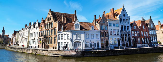 Panorama with canal and colorful traditional houses against cloudy blue sky in popular belgian destination, Bruges, Belguim