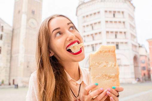 Young woman holding a piece of Parmesan cheese at the main square in Parma town in Italy. Parmesan is produced mostly in the province of Parma and was named after that producing region