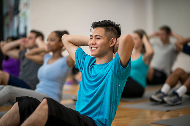 Abdominal Exercises in a Fitness Class A multi-ethnic group of adults are taking a fitness class together at the gym. They are doing sit-ups on their exercise mats. exercise class stock pictures, royalty-free photos & images