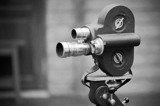 Retro movie camera on a tripod. Grain and noise added. Processed with black & white style,can be used for background