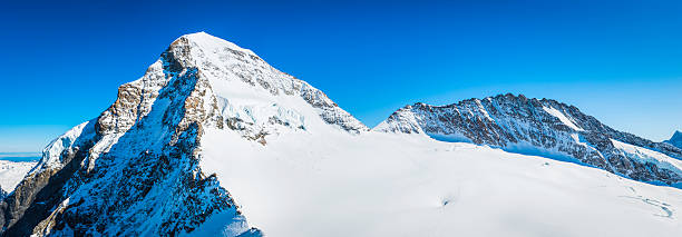 Switzerland Monch 4107m snowy mountain peak panorama Bernese Alps Jungfrau The snow capped summit and rocky ridges of The Monch (4107m) reaching into the deep blue mountain skies above the UNESCO World Heritage Site in the Alps of Switzerland. eiger northface stock pictures, royalty-free photos & images