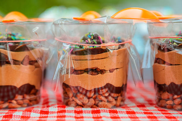 Pre Packaged Chocolate Creme Dessert in a glass. Layers of fine chocolate cream and chocolate raisins in a glass covered with plastic foil with orange spoon on top sitting on rustic red and white table cloth.