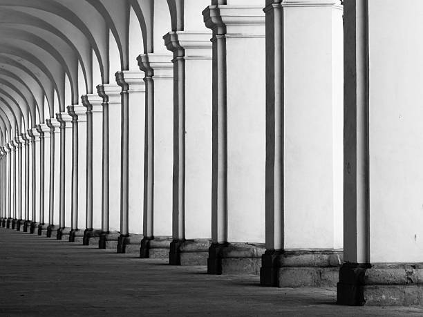Row of column in colonnade. Perspective view of long arc vault corridor. Black and white image.