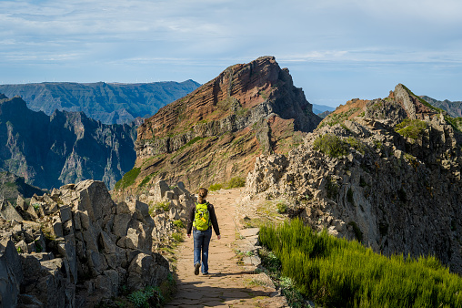 Woman hiker with green backpack doing her hike of Pico Arieiro to Pico Ruivo hiking route. Madeira island, Portugal.