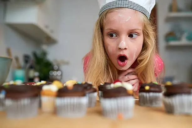 Shot of a surprised little girl looking at cupcakes she baked at home