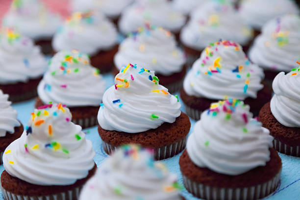 Tray of chocolate brown cupcakes with white cream and colorful icing