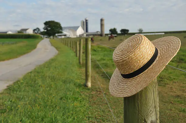 closeup of Amish straw hat laying over farm fence post
