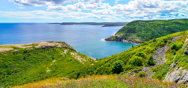 Sunny summer day over rocky coastline cliffs of Canadian National Historic site  Fort Amherst, St John's Newfoundland.  Cape Spear in background, people in distance hiking along the Cabot trail.