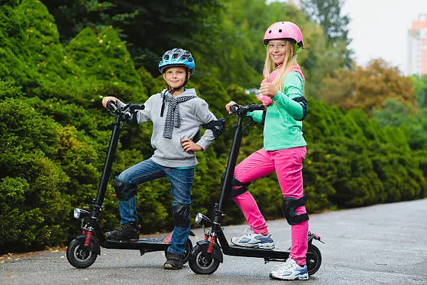 Happy kids standing on electric scooter outdoor.