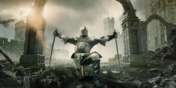 A medieval knight in a suit of armour, kneeling on knee holding up a sword in each outstretched hand. The knight is alone in front of a ruined medieval arch and outbuildings in front of a castle, surround by rocks and rubble under a dramatic stormy evening sky.