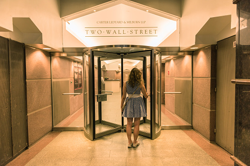 New York, USA - June 18, 2016: Young woman entering two wall street building with office of Carter Ledyard & Milburn LLP