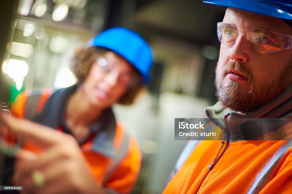 Industrial engineers two industrial service engineers conduct a safety check of a control panel and boiler room at a power station . They are both wearing safety equipment and are looking at a control panel trying to find the fault. Engineer Stock Photo