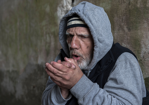 Portrait image of a mature homeless man rubbing his hands together trying to keep warm.