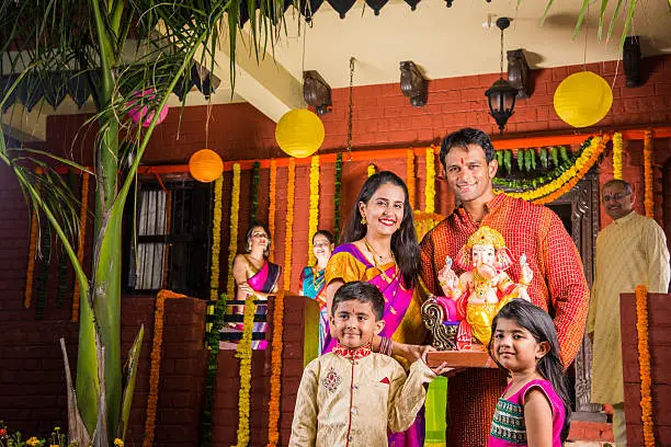 cheerful indian family welcoming lord Ganesha idol on ganesh festival or ganesh chaturthi on palkhi decorated with garland flowers