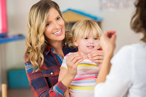 Mother and toddler daughter practice sign language Cute blonde toddler girl sitting on Caucasian mother's lap. Mother is smiling and practicing "more" sign language with daughter and preschool teacher. american sign language photos stock pictures, royalty-free photos & images