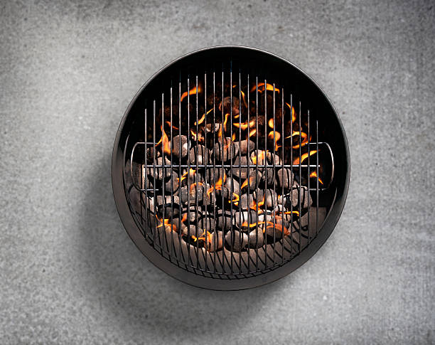 Top view of a grill with meat cuts out of focus in the background cooking on charcoal.