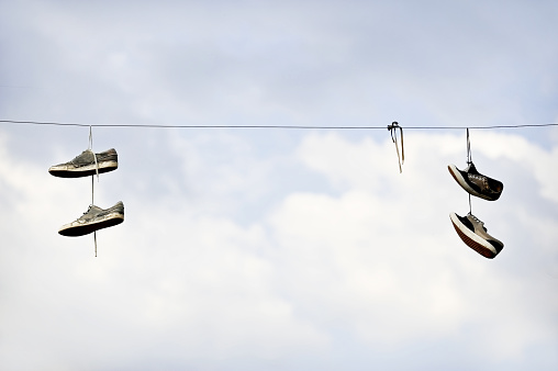 Two pairs of shoe laying on an electricity cable with blue sky on background