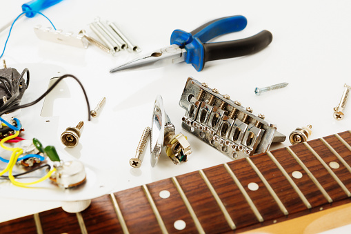 An electric guitar has been completely dismantled and now lies in pieces on a workbench with some hand tools.