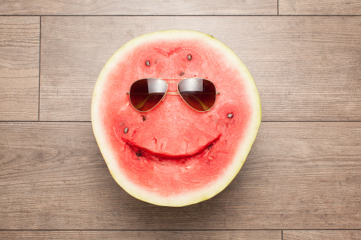 Smiling watermelon in sunglasses lying on a wooden floor