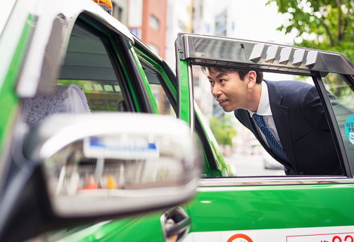 A man speaking to a taxi driver to give directions from a Tokyo street.