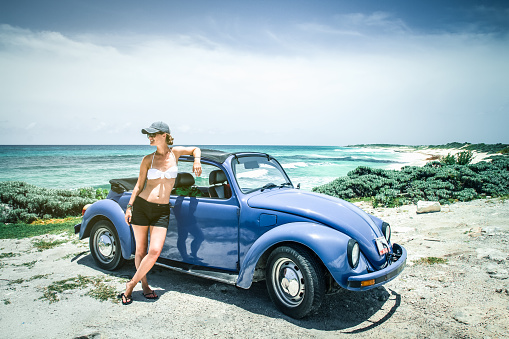 Cozumel, Yucatan, Mexico - July 22, 2012: Danish female, Mette Smedegaard Nielsen, leaning up against a convertible VW beetle on a remote beach on the island Cozumel in Mexico