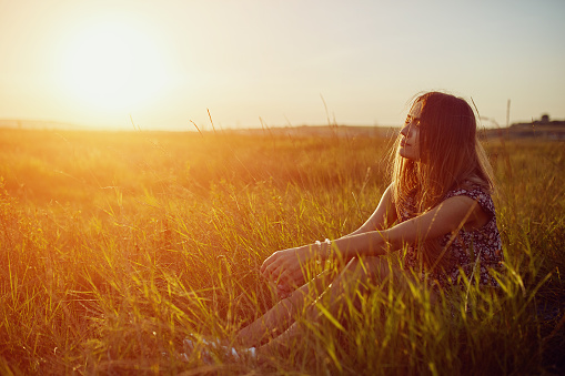 Beautyful teenage model girl outdoors enjoying nature. Resting on the field. Glow sun. Free happy woman. Toned in warm colors. Summer